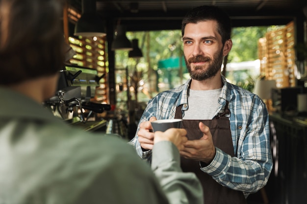 Portret Nieogolony Mężczyzna Barista Ubrany W Fartuch Uśmiechający Się Podczas Pracy W Ulicznej Kawiarni Lub Kawiarni Na świeżym Powietrzu
