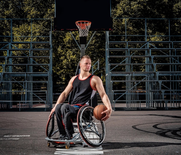 Portret niepełnosprawnego koszykarza na wózku inwalidzkim na otwartym boisku.