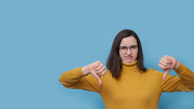 Portret niezadowolonej emocjonalnie studentki w okularach i żółtym swetrze z palcem skierowanym w dół