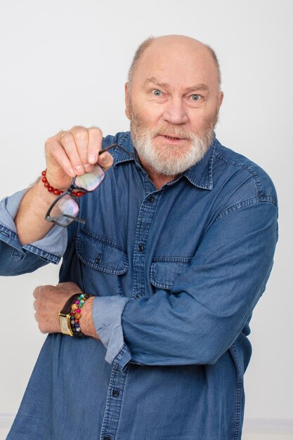 Portret oburzonego siwowłosego mężczyzny w dżinsowej koszuli na białym tle