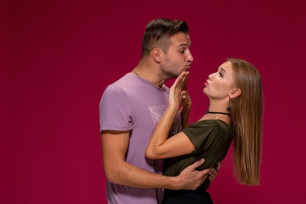 Portret oburzonej niezadowolonej kobiety gestem zatrzymania ręką, podczas gdy mężczyzna próbuje ją pocałować na bordowym tle