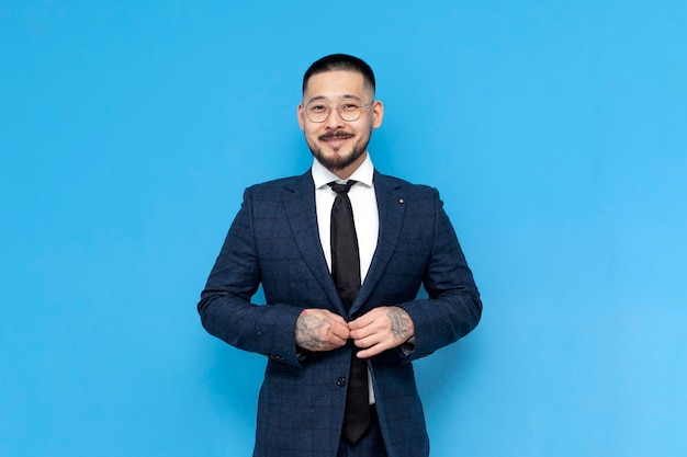portret odnoszącego sukcesy azjatyckiego biznesmena w garniturze i okularach na niebieskim, odizolowanym tle