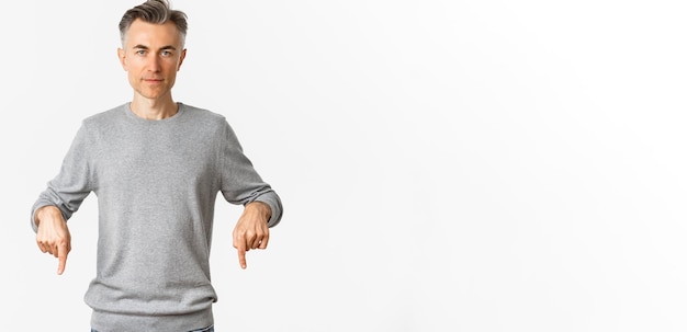 Zdjęcie portret odnoszącego sukcesy mężczyzny w średnim wieku w szarym swetrze, wskazującego palcami w dół i wyglądającego pewnie