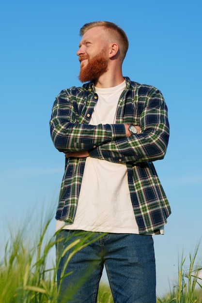 Portret odnoszącego sukcesy rolnika Mężczyzna stoi na polu pszenicy w koszuli i dżinsach Błękitne niebo w tle
