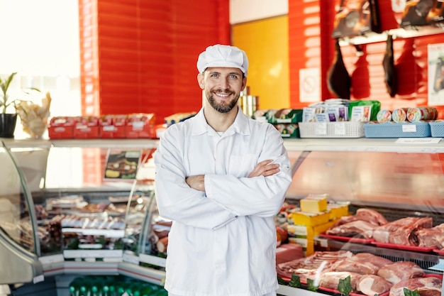 Portret odnoszącego sukcesy rzeźnika w sklepie mięsnym uśmiechającego się do kamery