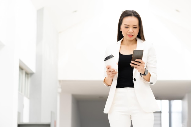 Portret odnoszącej sukcesy azjatyckiej bizneswoman w średnim wieku trzymającej smartfon i kawę uśmiechającą się do kamery