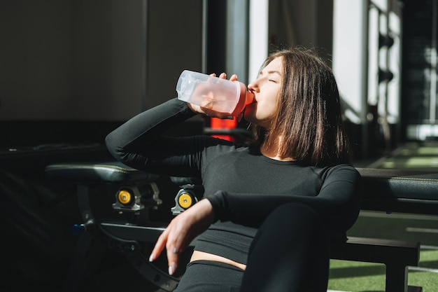 Portret odpoczywającej młodej kobiety brunetki w sporcie aktywnym nosić wodę pitną w siłowni klubu fitness