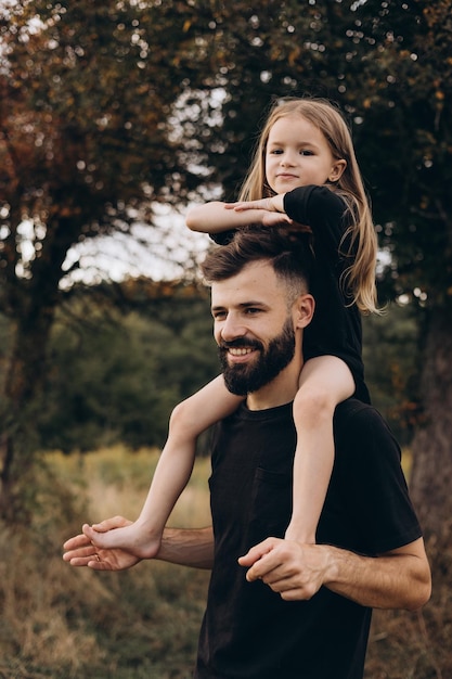 Portret ojca i dziecka Stylowy ojciec z brodą trzyma na ramionach dziecko mała dziewczynka obejmują się i uśmiechają radujcie się i bawcie szczęśliwy Dzień Ojca