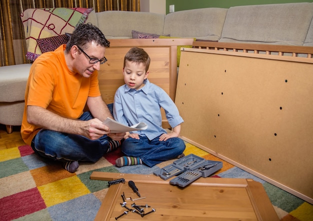 Portret ojca i syna z narzędziami czytającymi instrukcję montażu nowych mebli do domu. Koncepcja wypoczynku rodzinnego