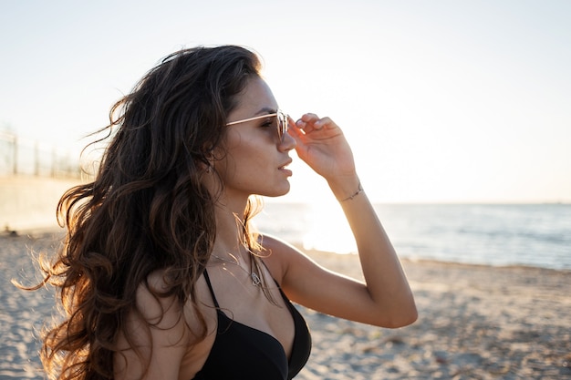 Portret olśniewającej Ciemnowłosej dziewczyny w okularach przeciwsłonecznych i czarnym staniku w pobliżu morza