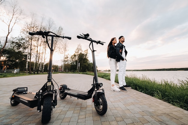 Zdjęcie portret pary siedzącej w pobliżu skuterów elektrycznych, ciesząc się razem na łonie natury, dwoje kochanków na skuterach elektrycznych