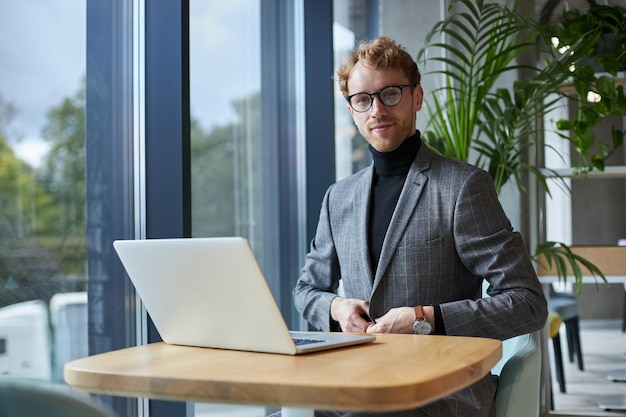 Portret pewnego siebie freelancera w stylowych okularach za pomocą laptopa pracującego w domu