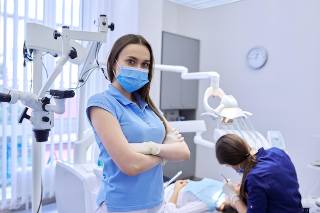 Portret pewnej siebie dentysty w masce medycznej ze skrzyżowanymi rękami, profesjonalny lekarz patrzący na kamerę w klinice dentystycznej