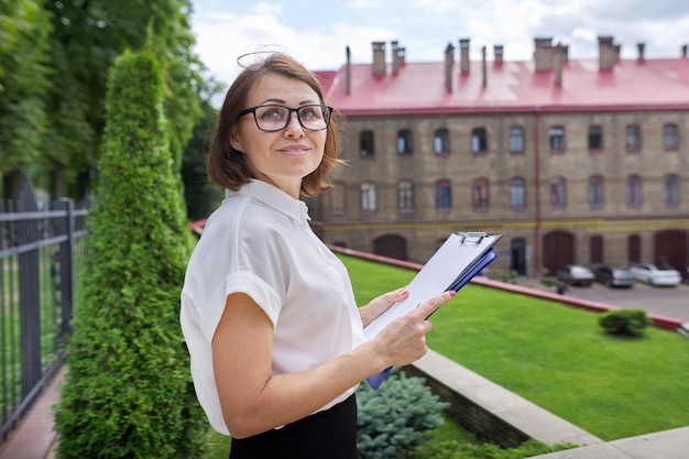 Portret pewnej siebie uśmiechniętej kobiety doradcy nauczycielki z papierowymi dokumentami w schowku