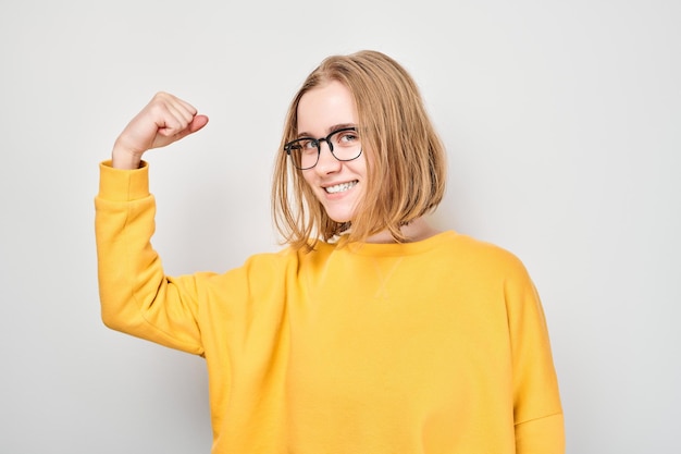 Portret pewnej studentki pokazującej biceps wykazujący siłę na białym tle studia Koncepcja szczęśliwego zwycięzcy