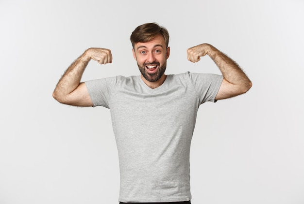 Portret pewnie brodaty mężczyzna zginając bicepsy, pokazując swoje mięśnie po treningu na siłowni, stojąc
