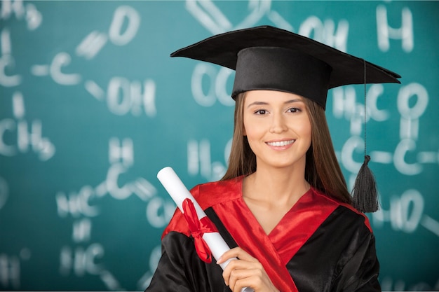 Portret pewność studentki w sukni ukończenia szkoły pokazując świadectwo na tle.