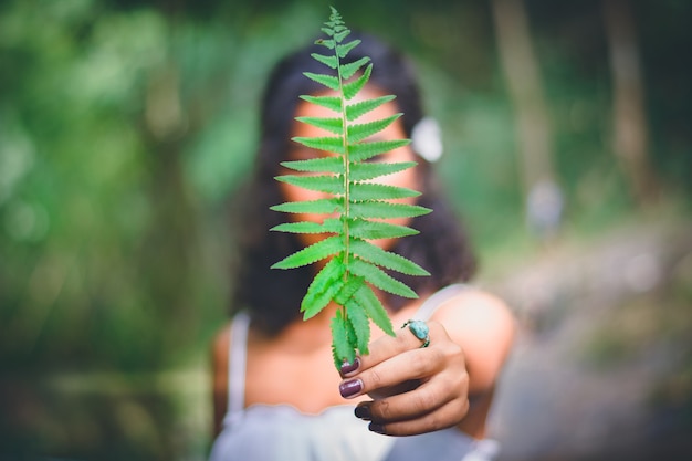 Portret piękna Azjatycka kobieta trzyma zielonego liść przed jej twarzą; cieszyć się naturalnym na zewnątrz