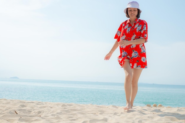 Zdjęcie portret piękna młoda azjatycka kobieta relaksuje spacery wokół oceanu na plaży z białą chmurą na niebieskim niebie w podróży wakacje