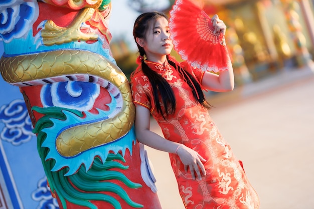 Portret piękne słodkie uśmiechy Młoda azjatycka kobieta ubrana w czerwoną, tradycyjną chińską dekorację cheongsam i trzymająca chińskie wachlowanie na festiwal chińskiego nowego roku w chińskiej świątyni w Tajlandii