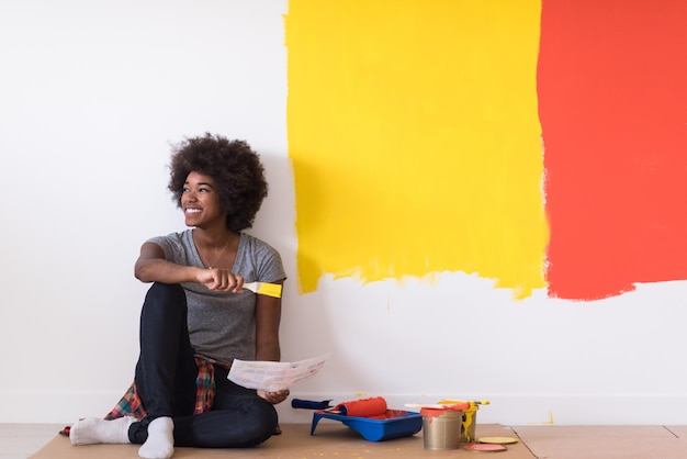 Portret pięknej african american kobieta malarz siedzi na podłodze przy ścianie po malowaniu.