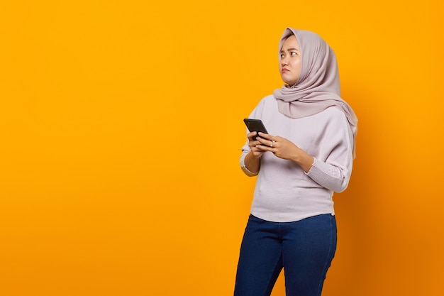 Portret pięknej azjatyckiej kobiety trzymającej telefon komórkowy i patrzącej na bok na żółtym tle