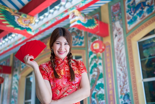 Portret pięknej azjatyckiej kobiety w sukience Cheongsam z czerwoną kopertą w rękuTajlandia ludzieSzczęśliwego chińskiego nowego roku koncepcja