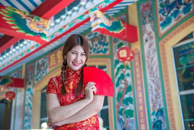 Portret pięknej azjatyckiej kobiety w sukience Cheongsam z czerwoną kopertą w rękuTajlandia ludzieSzczęśliwego chińskiego nowego roku koncepcja