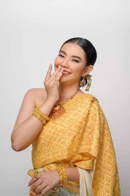 Portret pięknej azjatyckiej kobiety w tradycyjnym tajskim stroju, uśmiech i użyj dłoni, zamknij usta z wdzięczną pozą na białej ścianie