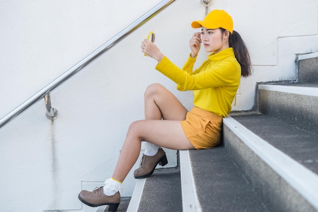 Portret pięknej azjatyckiej kobiety w żółtym ubraniuDziewczyna hipsterów nosi żółty kapelusz siedzi na schodach, aby zrobić zdjęcieTajlandczycy ludzie