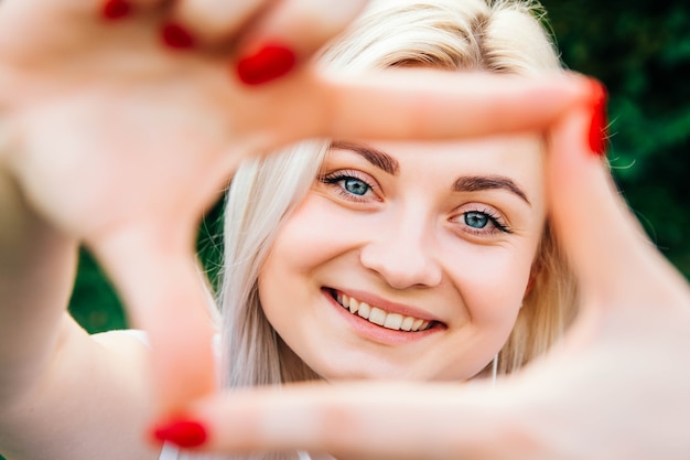 Zdjęcie portret pięknej blondynki dziewczyna uśmiecha się robiąc ramę rękami i palcami ze szczęśliwą twarzą