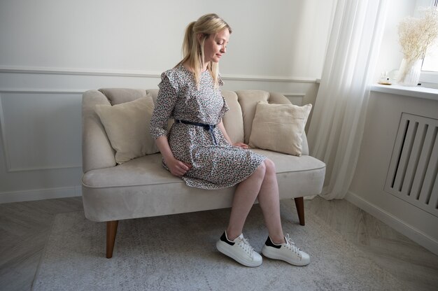 Portret pięknej blondynki w sukience, siedząc na kanapie.