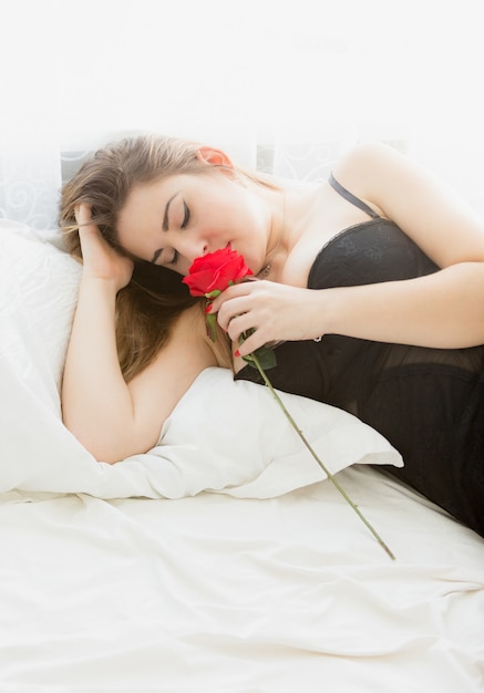 Portret pięknej brunetki kobiety pozującej z czerwoną różą w łóżku