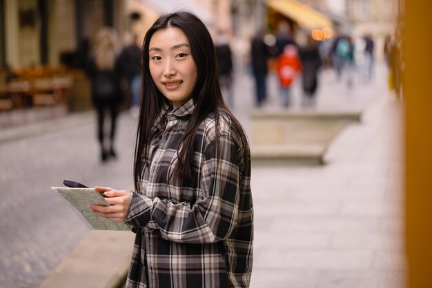 Portret pięknej brunetki Koreanki trzymającej mapę i porównującej ją z nawigacją smartfona na ulicach starego miasta Azjatycka turystka podróżująca po Europie