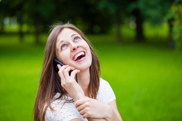 Portret pięknej brunetki rozmawiającej przez telefon komórkowy w letnim zielonym parku
