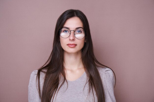 Portret pięknej brunetki w okularach i poważnym wyrazie twarzy na białym tle w brązowym tle studyjnym