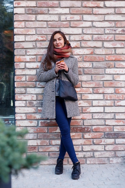 Portret pięknej brunetki z napojem na wynos na ulicy szalik i jesienny płaszcz w