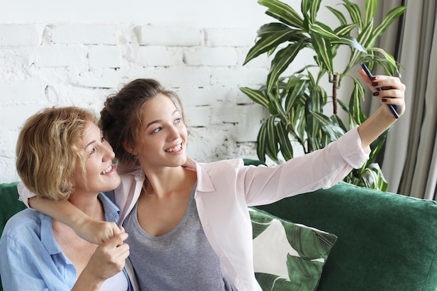 Portret pięknej dojrzałej matki i jej córki robiące selfie za pomocą smartfona i uśmiechniętego do domu i szczęśliwego