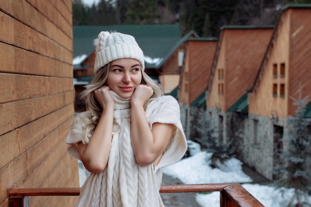 Portret pięknej dziewczyny w białym kapeluszu i swetrze na ulicy na balkonie Ciepłe zimowe ubrania