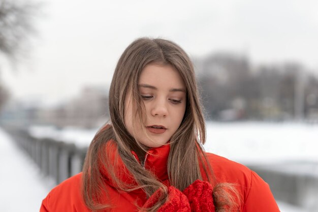 Portret pięknej dziewczyny w czerwonej kurtce i czerwonych rękawiczkach z dzianiny Młoda kobieta w ciepłych ubraniach na zewnątrz w winter park