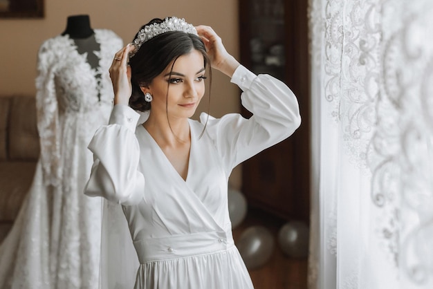 Portret pięknej dziewczyny w szlafroku z koroną na głowie koncepcje mody glamour Poranek panny młodej panna młoda w szlafrok stoi w pobliżu manekina z sukienką ślubną
