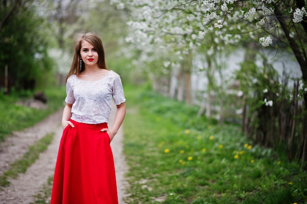 Portret pięknej dziewczyny z czerwonymi ustami w ogrodzie kwiat wiosna, nosić na czerwoną sukienkę i białą bluzkę.