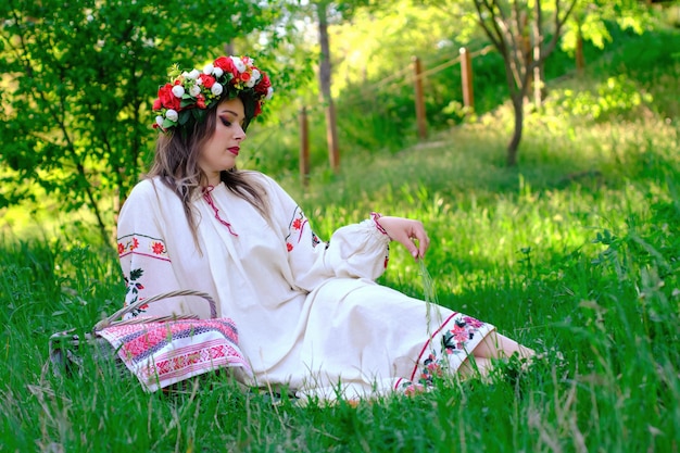 Portret pięknej dziewczyny z wieńcem w ukraińskich strojach narodowych leży na trawie na łące