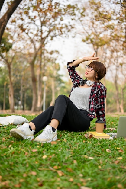 Portret pięknej i zrelaksowanej młodej azjatyckiej kobiety siedzącej na trawie w parku zieleni