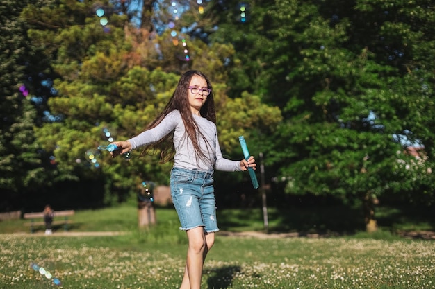 Portret pięknej kaukaskiej dziewczyny dmuchającej bańki mydlane z kolorowym bokeh machającym różdżką