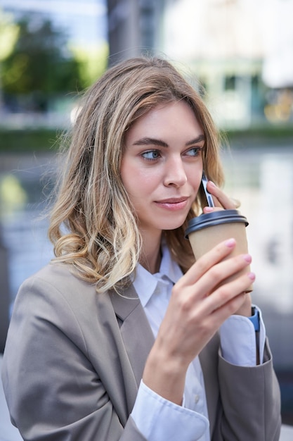 Portret pięknej kobiety rozmawiającej przez telefon komórkowy i pijącej kawę bizneswoman pije takeawa