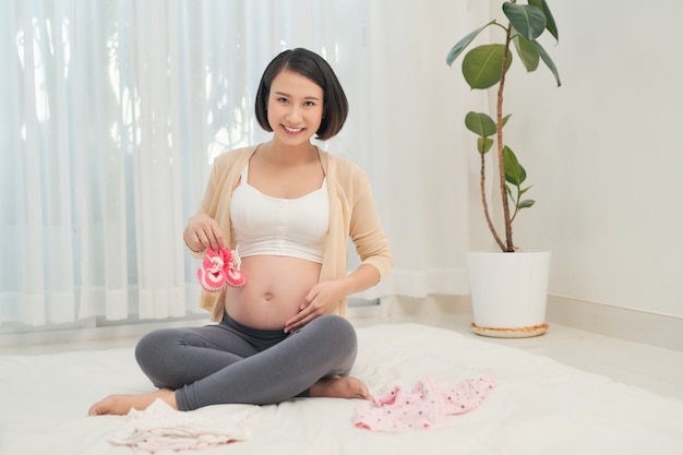 Portret pięknej kobiety w ciąży z ubraniami jej przyszłego dziecka