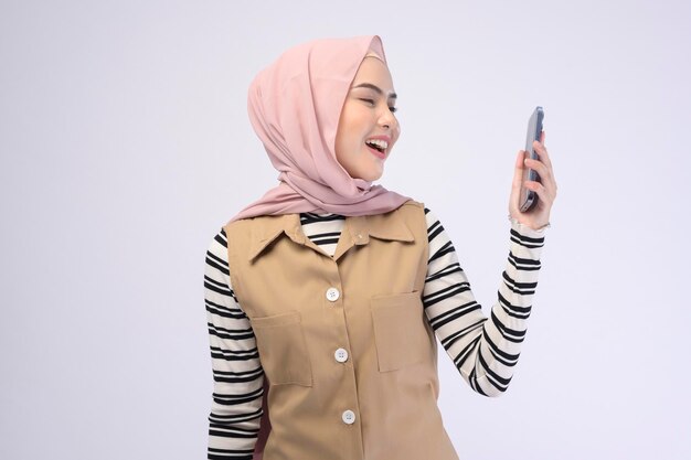 Portret pięknej kobiety w hidżabie używającej telefonu komórkowego na białym tle