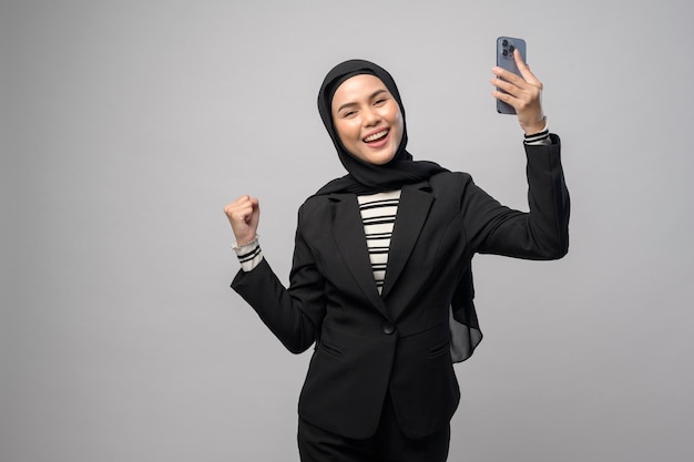 Portret pięknej kobiety w hidżabie używającej telefonu komórkowego na białym tle