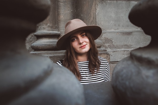 Portret pięknej kobiety w kapeluszu i koszuli w paski patrząc w kamerę na tle starego domu